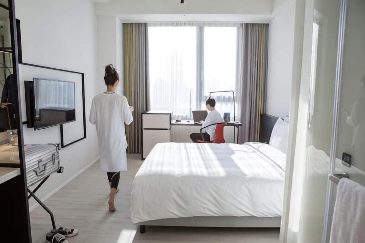 A hotel room with a bed, a desk with a laptop, a television, and a window with curtains.