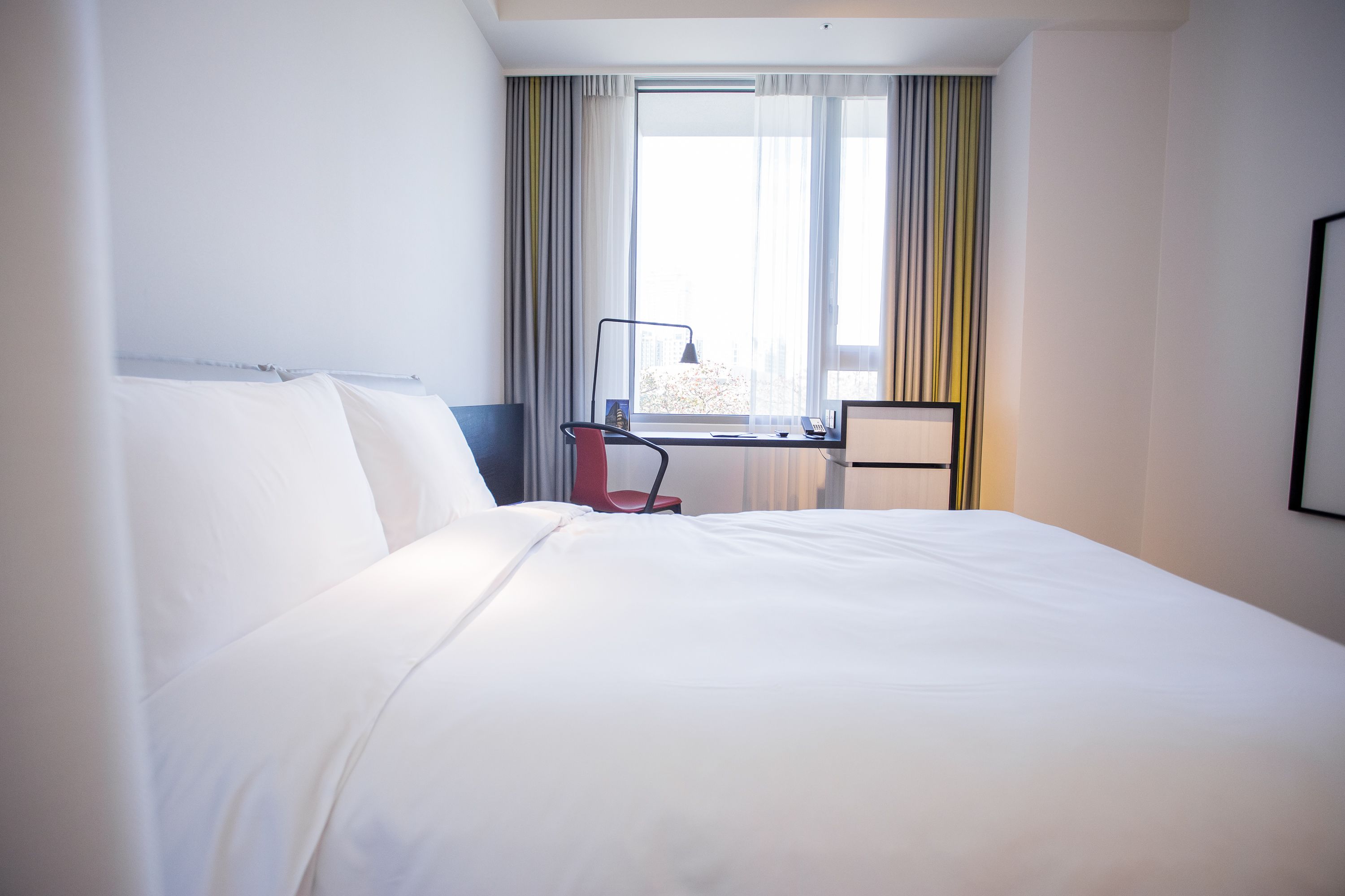 Una habitación de hotel con una cama grande, un escritorio con silla, una ventana con cortinas y vistas a la ciudad.