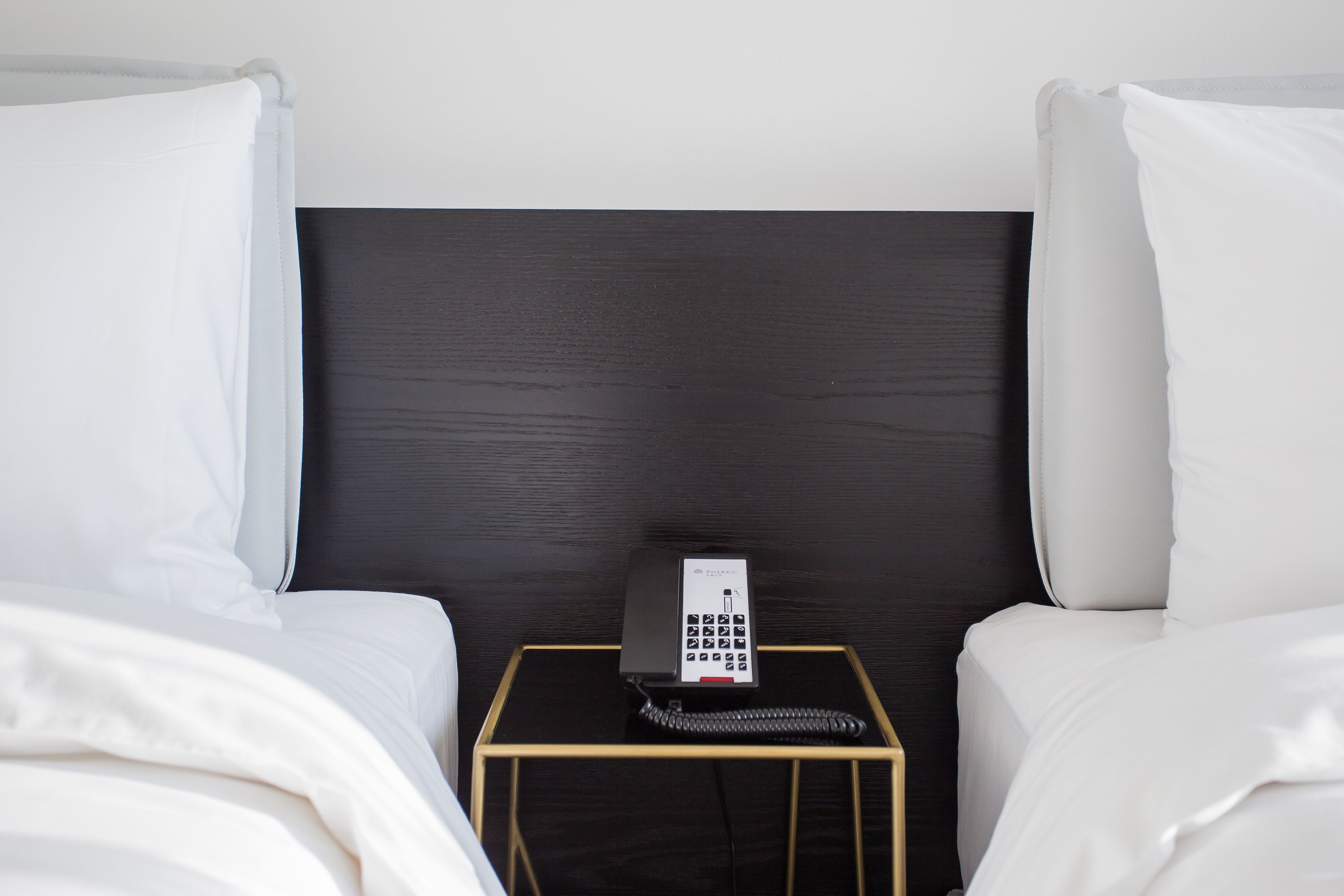 A hotel room with a bed, a bedside table with a telephone, and a dark headboard.