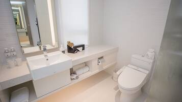 A modern bathroom with a white sink, mirror, and toilet. There are towels and toiletries on the counter.