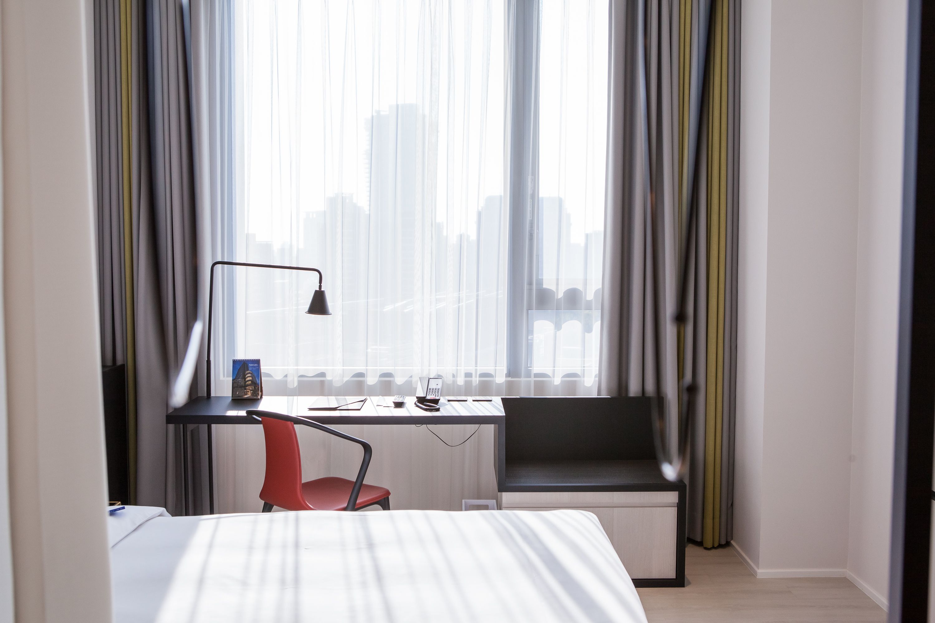 Une chambre d’hôtel comprenant un lit, un bureau avec une chaise, un téléphone et une fenêtre avec des rideaux.