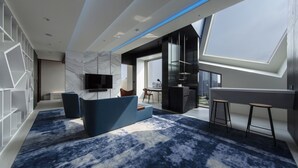 Una sala de estar moderna con alfombra azul, un televisor de pantalla plana y un ventanal con vistas a un paisaje urbano.