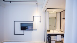 Habitación de hotel moderna con una cama grande, un televisor de pantalla plana en la pared, un baño con un espejo amplio y un diseño minimalista.