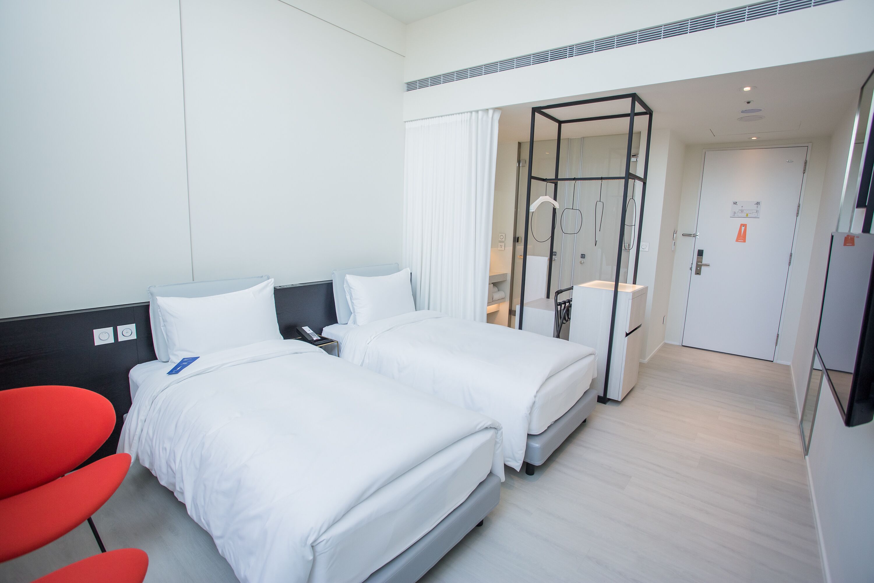 Habitación de hotel con dos camas, una silla roja, un escritorio y un panel de vidrio.