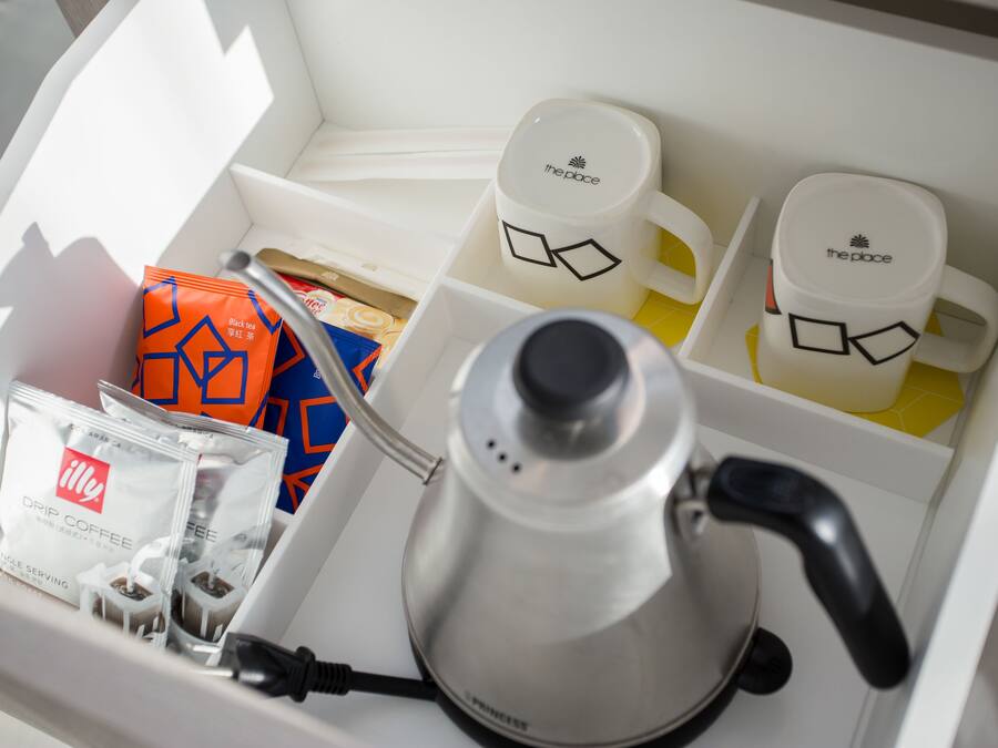 A coffee maker, two coffee cups, a tea bag, and a box of drip coffee in a compartment.