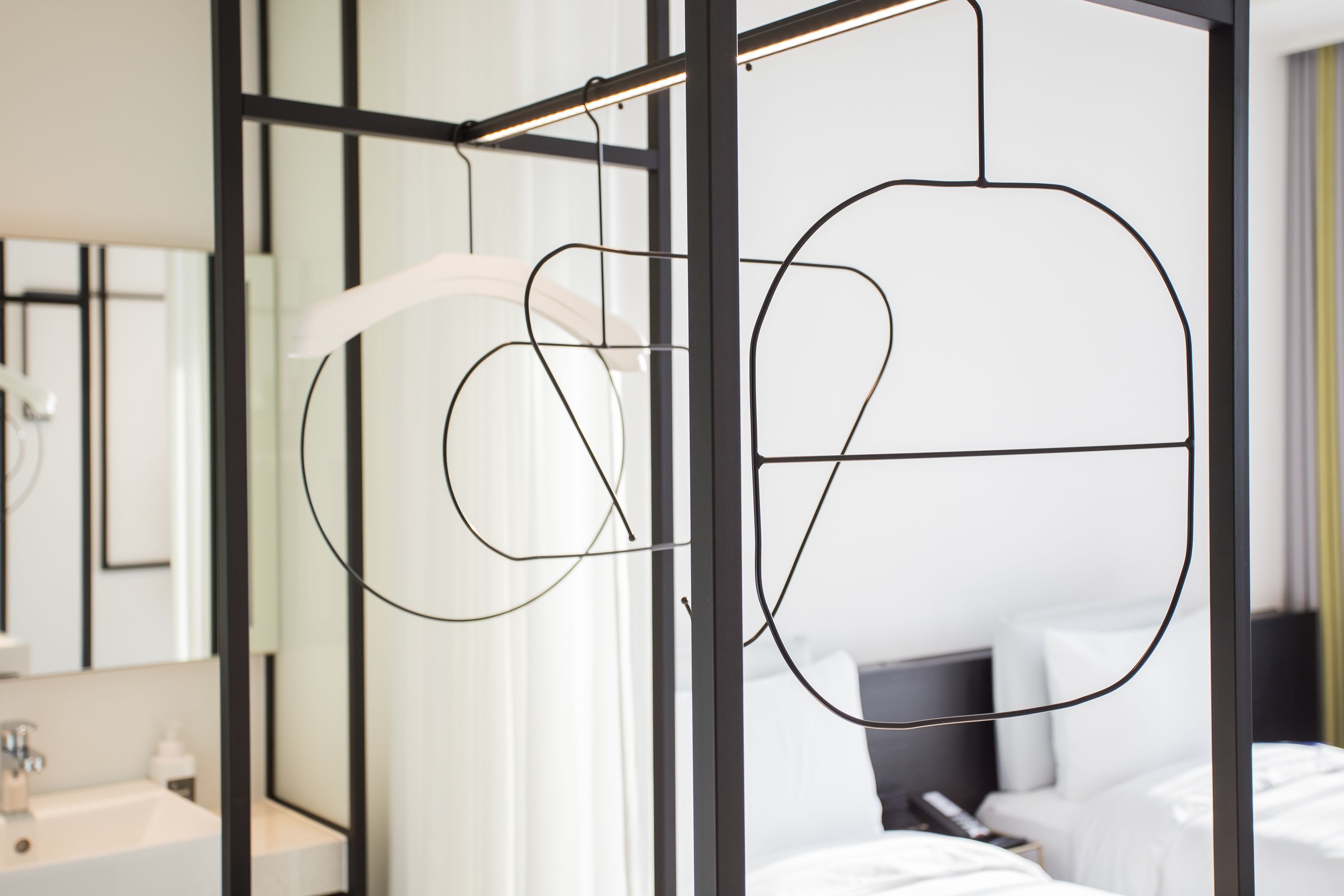 A modern hotel room with a minimalist design, featuring a large bed, a bedside table, and a bathroom with a mirror and sink.