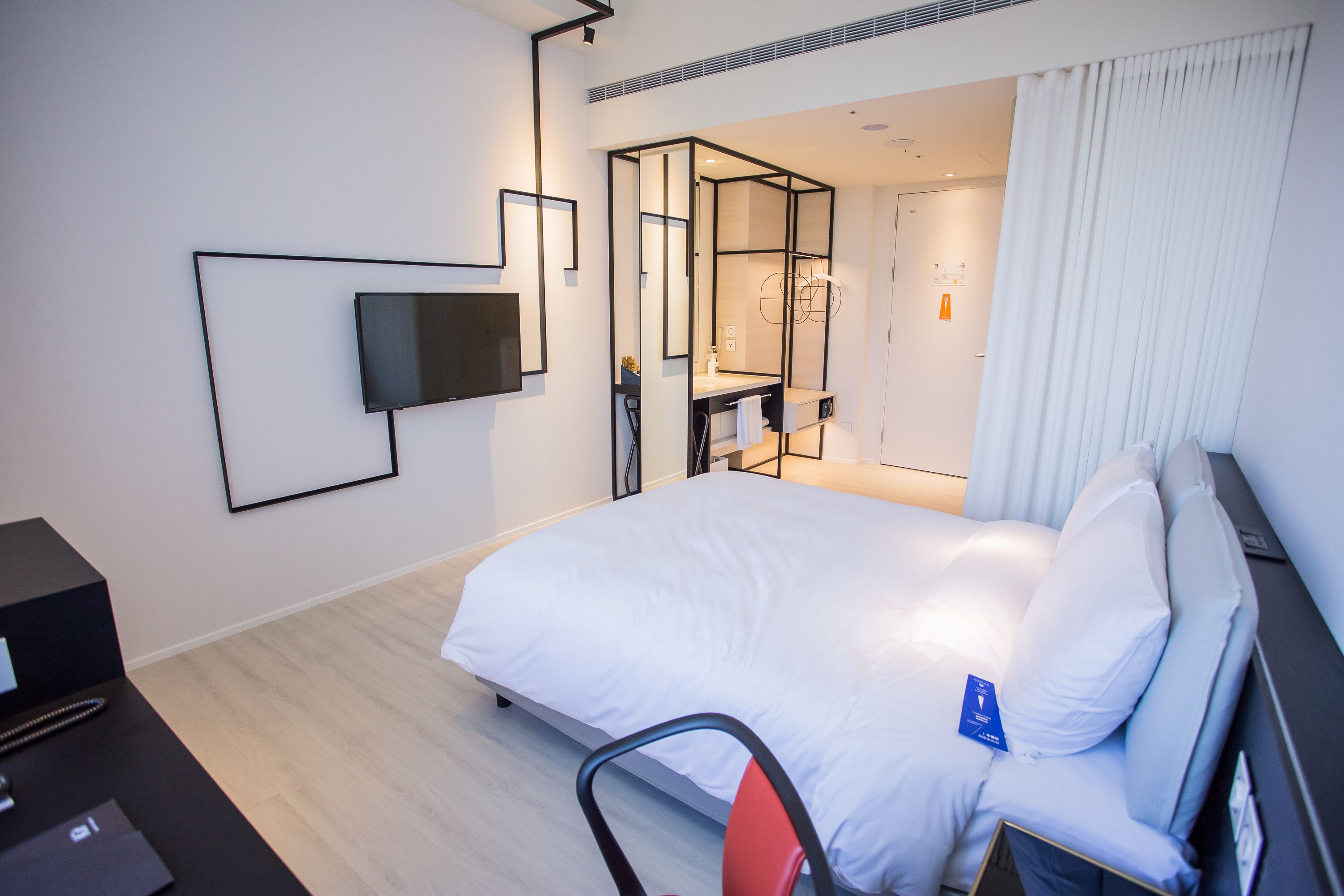 Una habitación de hotel moderna con una cama grande, un televisor de pantalla plana en la pared, un escritorio con una computadora y un espejo.