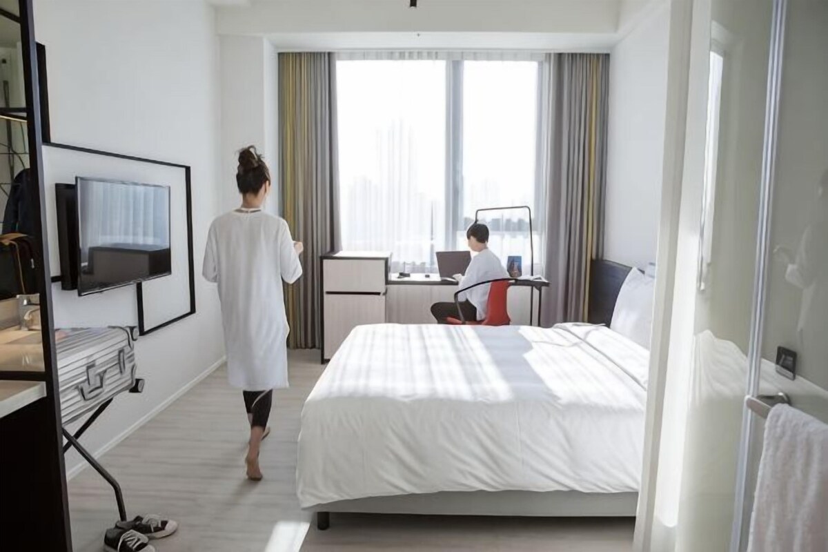 Una habitación de hotel con una cama, un escritorio con una computadora portátil, un televisor y una ventana con cortinas.