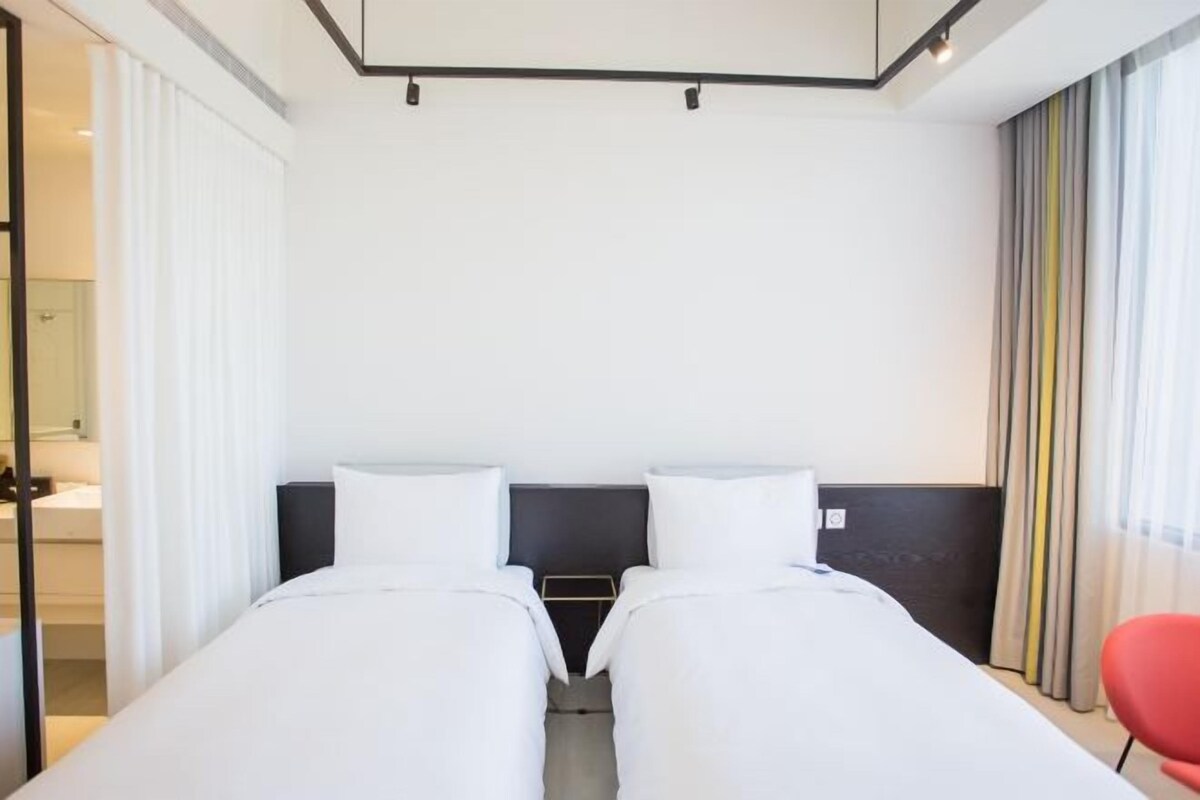 Een hotelkamer met twee eenpersoonsbedden, een tafeltje en een rode stoel.