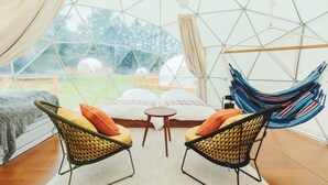 A cozy tented room with a bed, two wicker chairs, a small table, and a hammock.