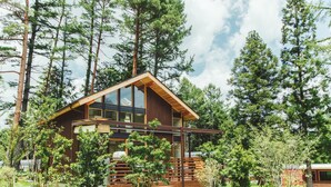 A wooden cabin with large windows, surrounded by trees and a grassy area.