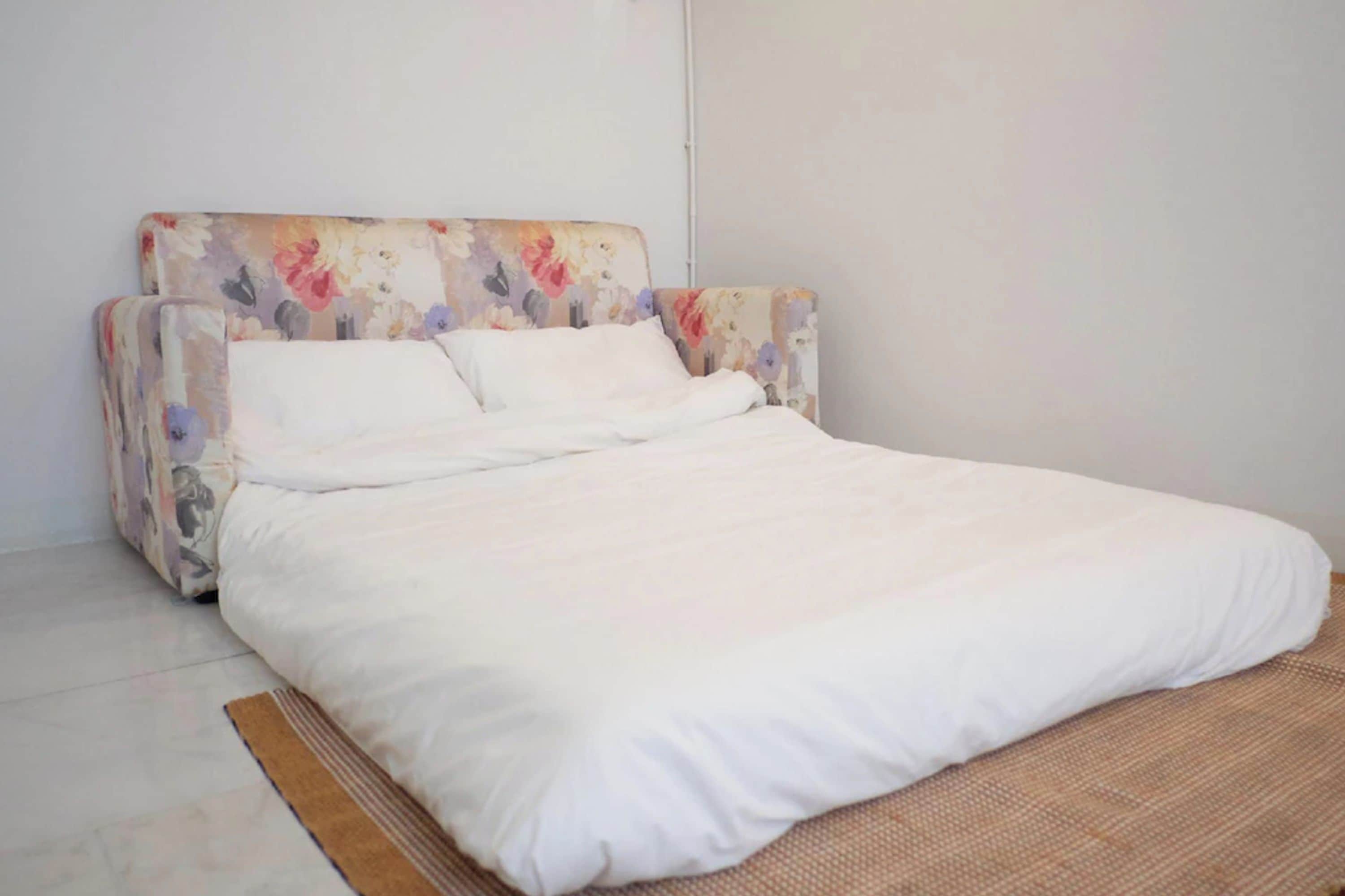 Un lit avec un matelas et des oreillers blancs, une tête de lit à motifs floraux et un mur uni.