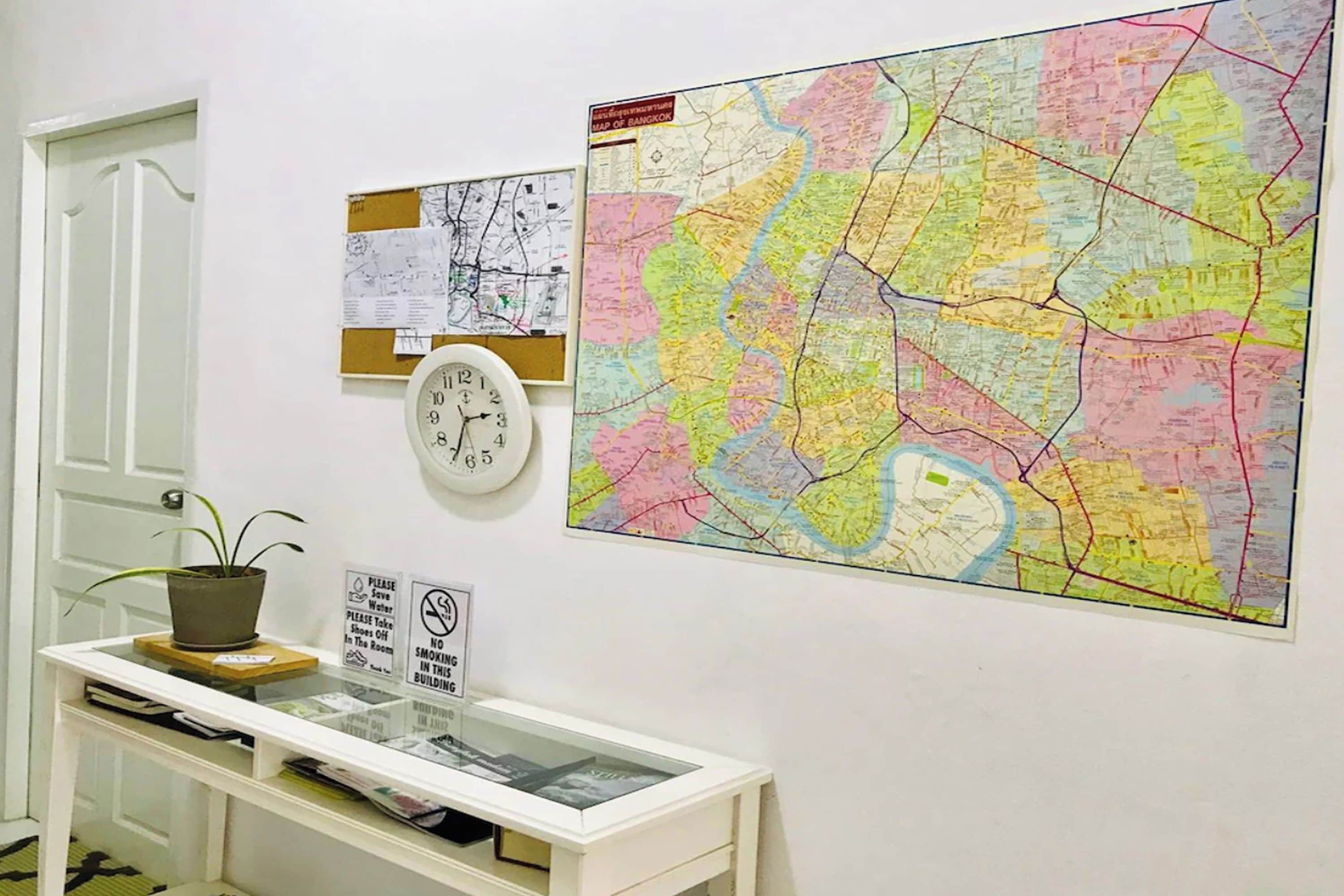 A wall with a large colorful map, a clock, and a small plant on a shelf.
