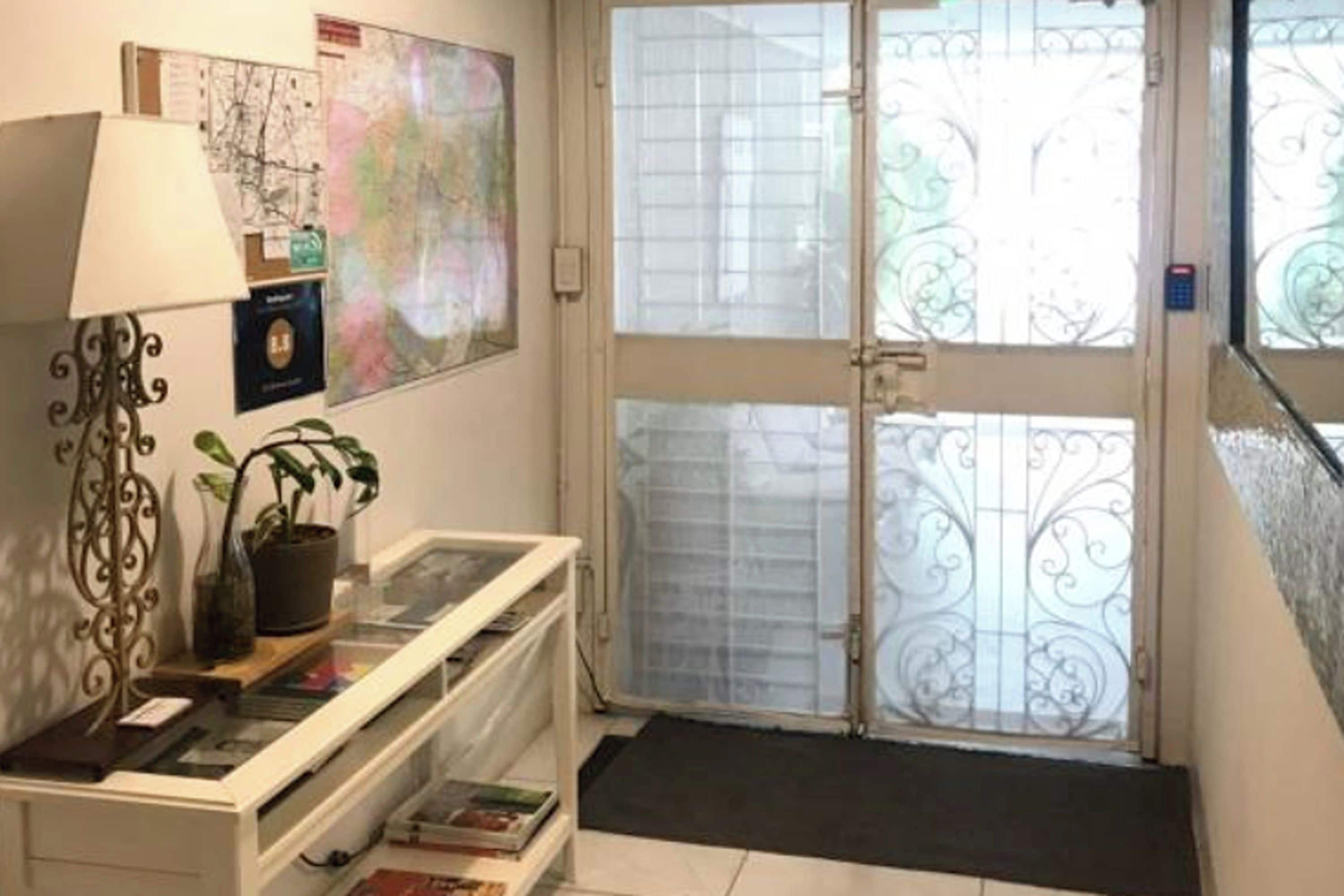 A room with a desk, a lamp, a potted plant, and a window with decorative ironwork.