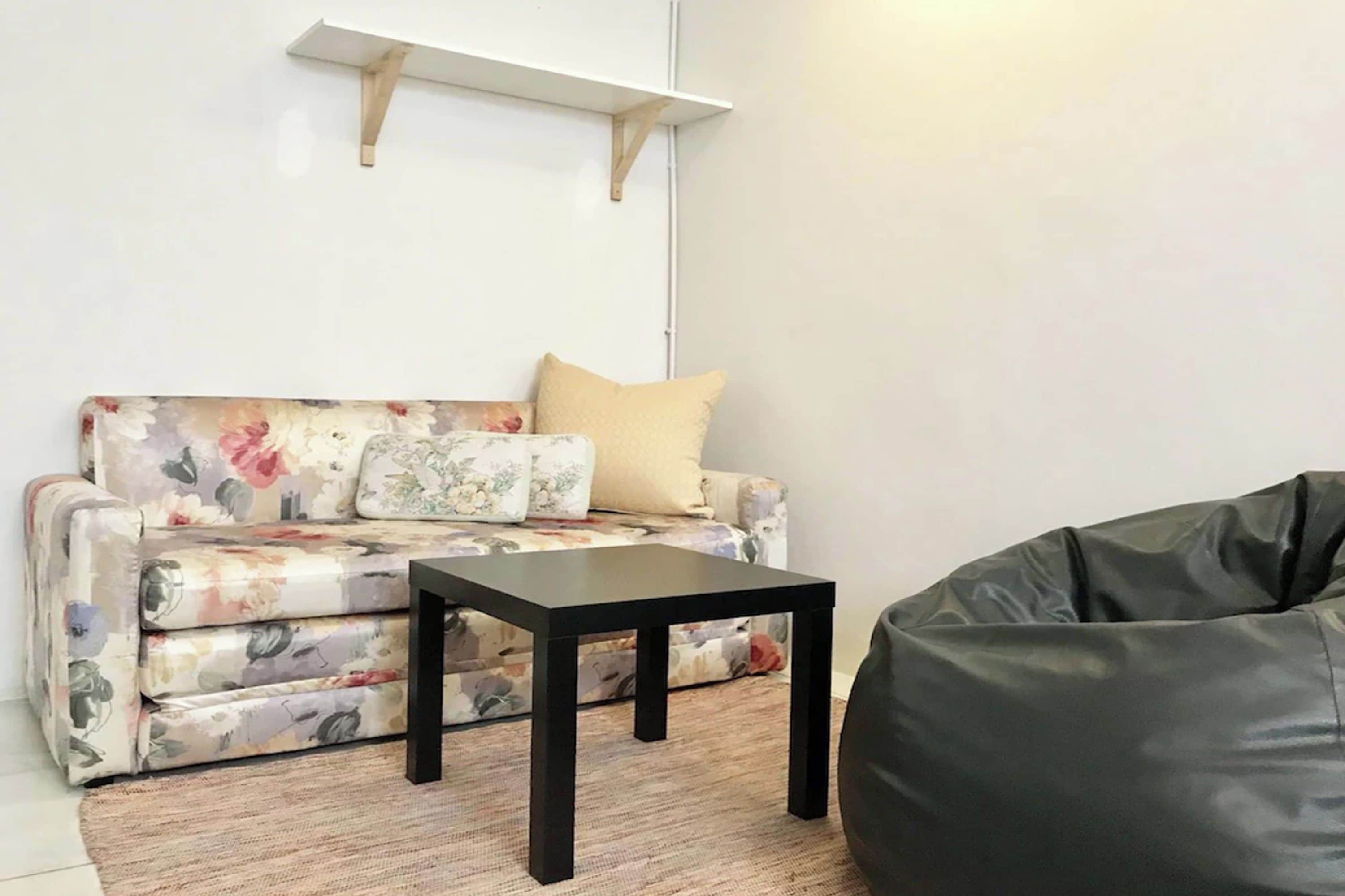 A living room with a floral sofa, a black coffee table, and a black bean bag.