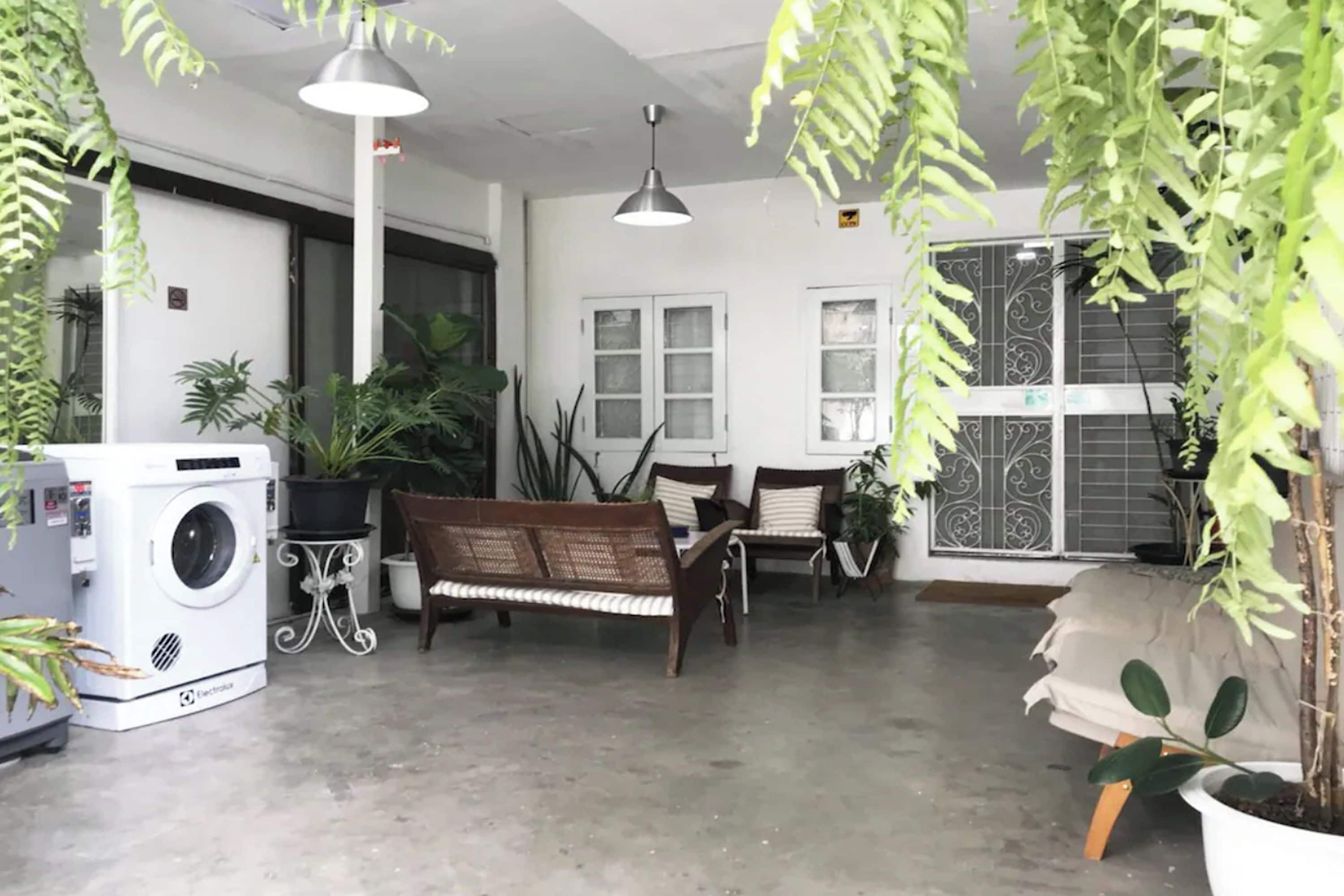 Habitació amb rentadora, una banca, taula i plantes en testos.