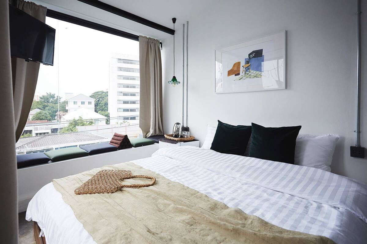 A hotel room with a large bed, a view of the city, a flat-screen TV, and a framed artwork on the wall.