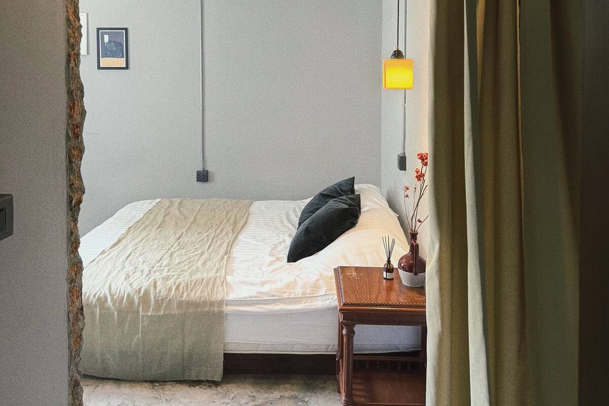 A bedroom with a bed, bedside table, lamp, and a picture on the wall.