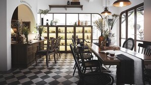 Un coin repas avec un sol à carreaux, des chaises en bois, une table sur laquelle se trouve une tasse, et un buffet aux portes vitrées.