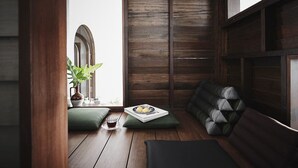 Une pièce chaleureuse avec un plancher en bois, un banc vert rembourré, une plante en pot et une petite table sur laquelle se trouvent un livre et une tasse.