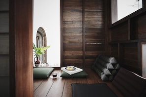 Una habitación acogedora con piso de madera, un banco tapizado en verde, una planta en maceta y una pequeña mesa con un libro y una taza.