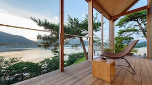 A wooden deck with a hammock and a small table, overlooking a lake and mountains. - Bayclub (Namhae)