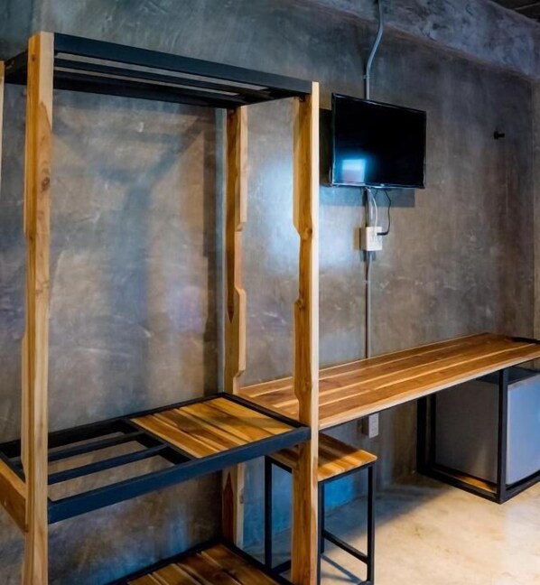 Una habitación minimalista con un banco de madera, un televisor fijado a la pared y suelo de hormigón.