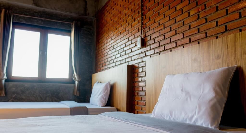 A room with two beds, a brick wall, and a window with curtains.