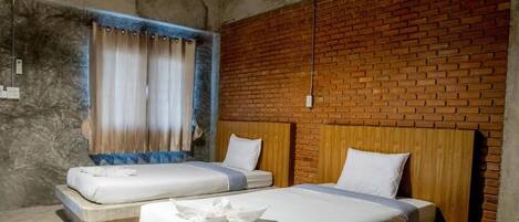 A room with two beds, a brick wall, and a window with curtains.