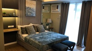 Un dormitorio moderno con una cama grande, mesitas de noche, un escritorio pequeño y una ventana con cortinas.