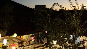 An outdoor patio area with wooden pergolas, hanging lights, and a seating area. - Omah Njonja Bed & Brasserie (Depok)