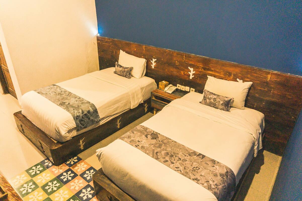 Two single beds with wooden headboards, a small bedside table with a telephone, and a patterned floor.