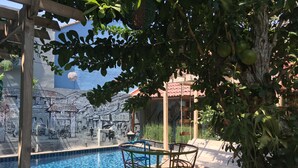 A poolside area with a mural, a swing chair, and a table. - Omah Njonja Bed & Brasserie (Depok)