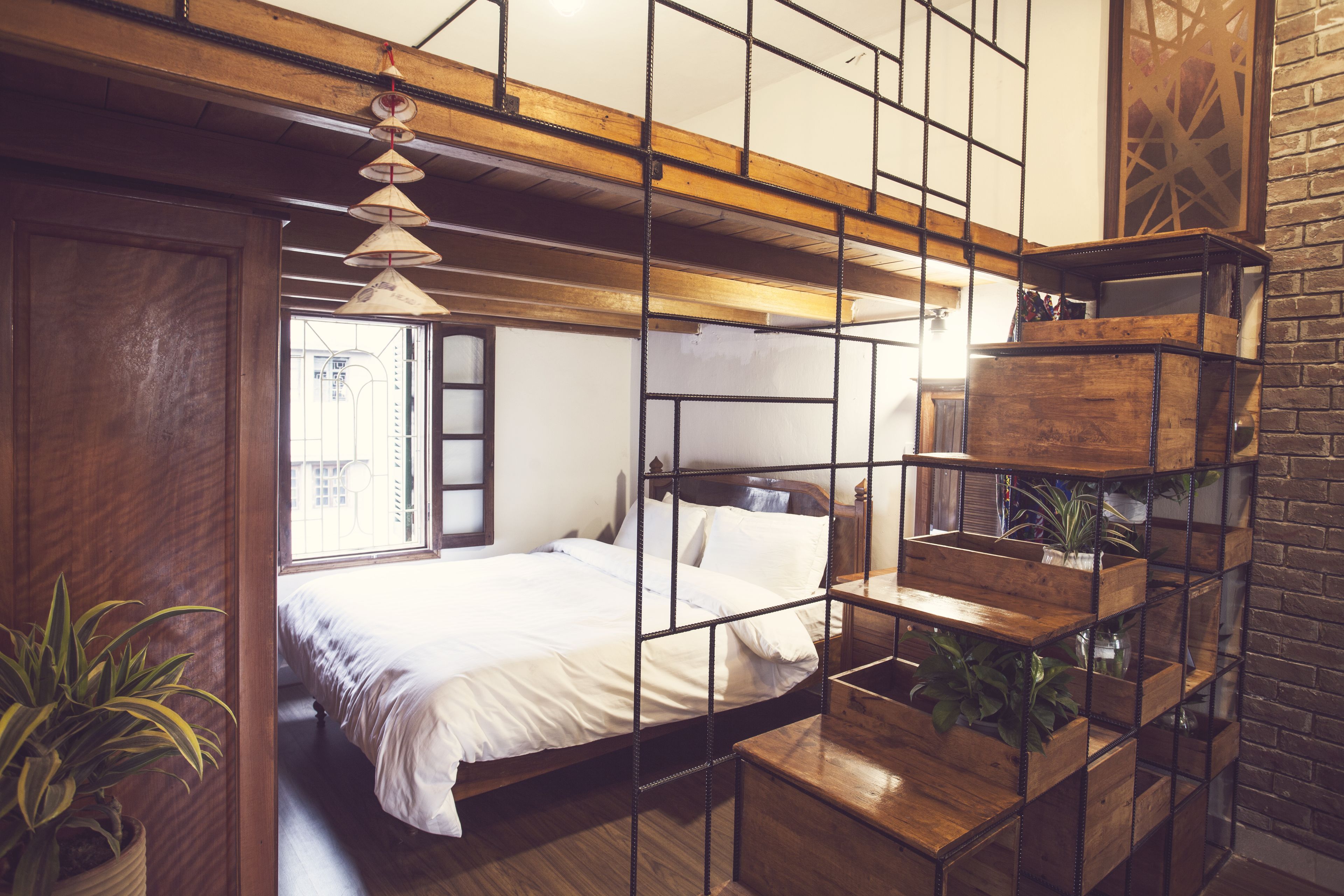 A bedroom with a wooden bed, a hanging light fixture, and a brick wall.
