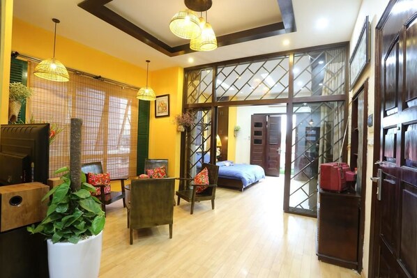 A room with a wooden floor, a bed with a blue bedspread, a chair, a table, and a potted plant.