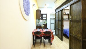 A narrow hallway with a dining area featuring a table with chairs and a floral tablecloth. There is a kitchen area with a refrigerator and a sink visible in the background. - Tuti Lakeside Homestay (Hanoi)
