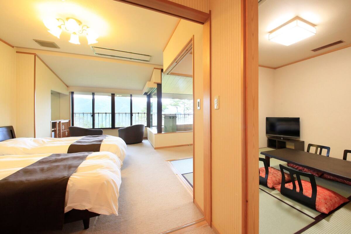 Quarto de hotel com cama, televisão, mesa de jantar com cadeiras e vista para o exterior.