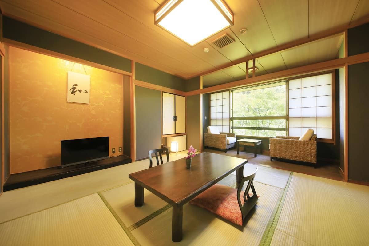 Um quarto japonês tradicional com tatames, uma mesa baixa e uma televisão.