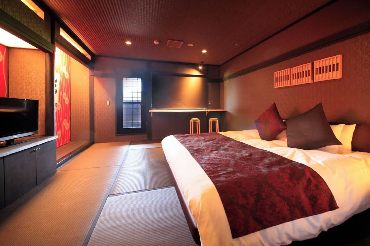 Quarto de hotel com cama, televisão em móvel, janela e parede com painel decorativo.