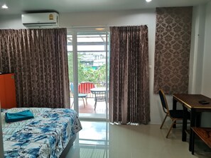 A hotel room with a bed, a table, a chair, and a balcony with curtains. - Mae-Porn Hostel (Takua Pa)