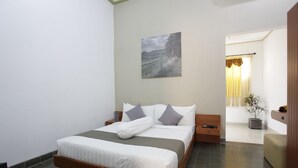 Un dormitorio ordenado con cama, mesitas de noche, una planta en maceta y un cuadro en la pared.