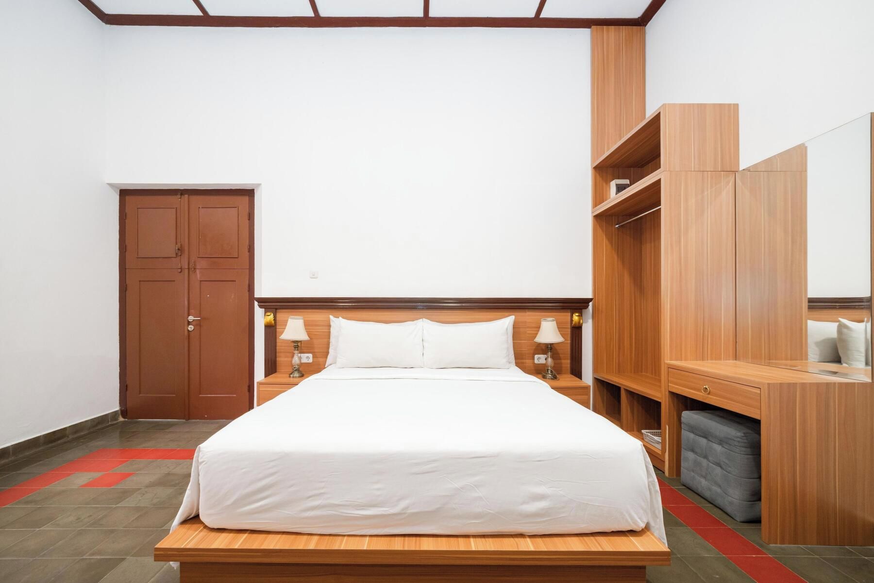 A hotel room with a wooden bed, a wardrobe, a mirror, and a desk.