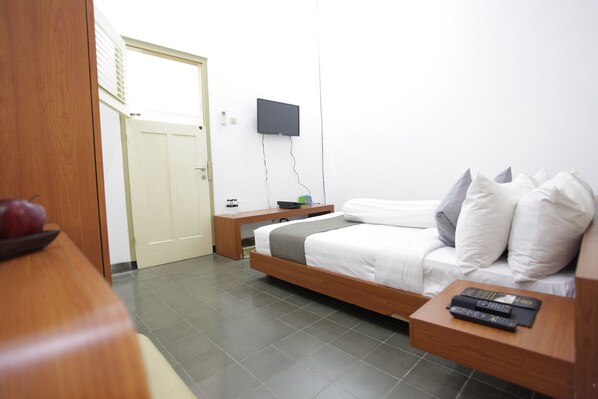 A hotel room with a bed, a bedside table with a remote control, a TV mounted on the wall, and a door leading to another room. - Taman Yuwono Heritage Malioboro by Natt's Hospitality (Yogyakarta)