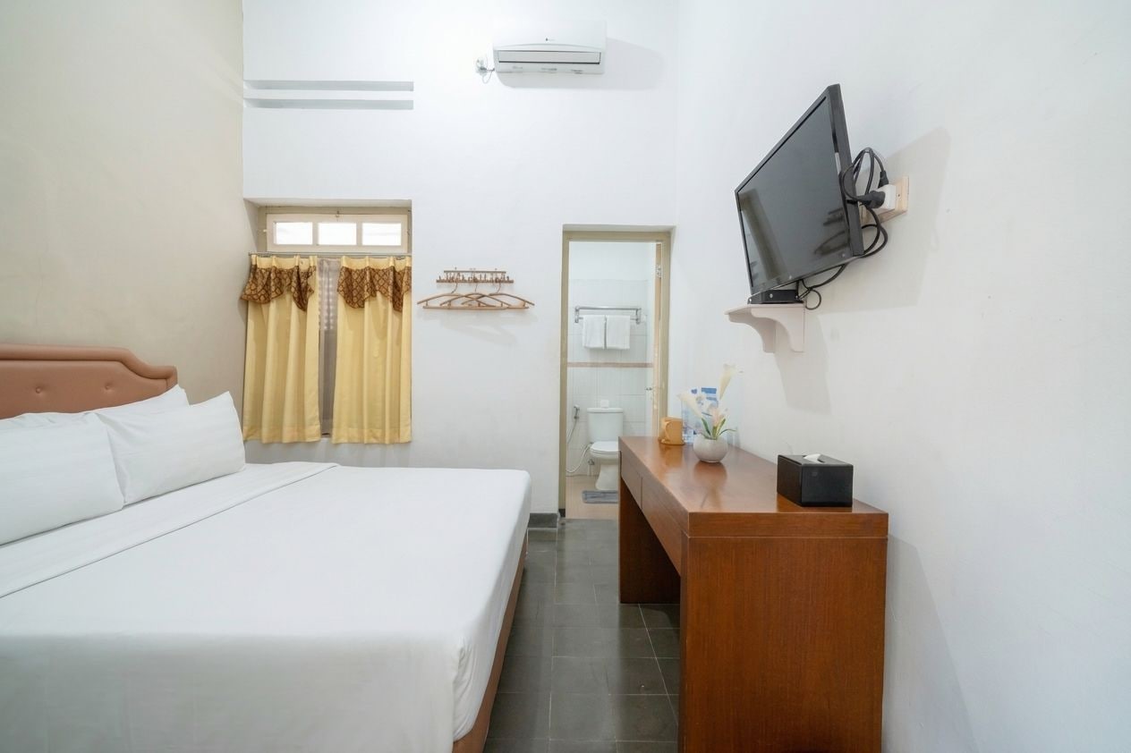 A hotel room with a bed, a desk, a television, and a bathroom visible through an open door.