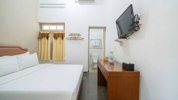 A hotel room with a bed, a desk, a television, and a bathroom visible through an open door.
