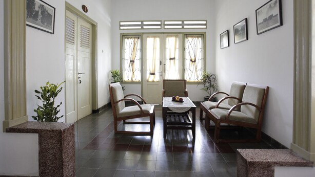 A room with a reception desk, two chairs, a table, and a door. - Taman Yuwono Heritage Malioboro by Natt's Hospitality (Yogyakarta)