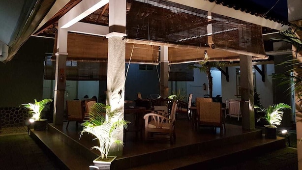 Un patio techado al aire libre con mesas y sillas, rodeado de plantas en macetas.