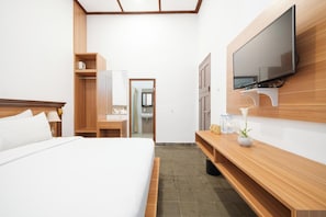 A hotel room with a bed, a wooden desk, a television mounted on the wall, and a bathroom visible through an open door.