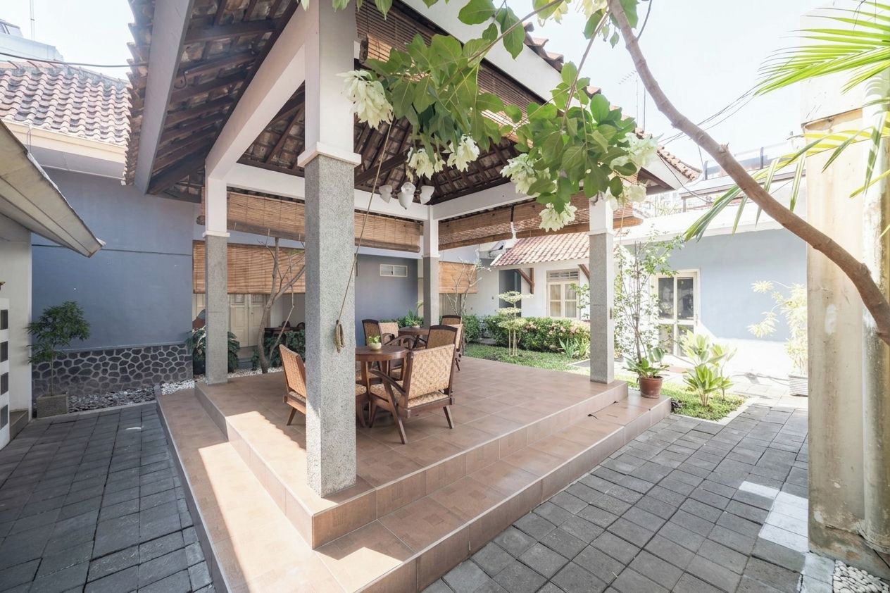 A covered patio area with a table and chairs, surrounded by plants and a stone wall.