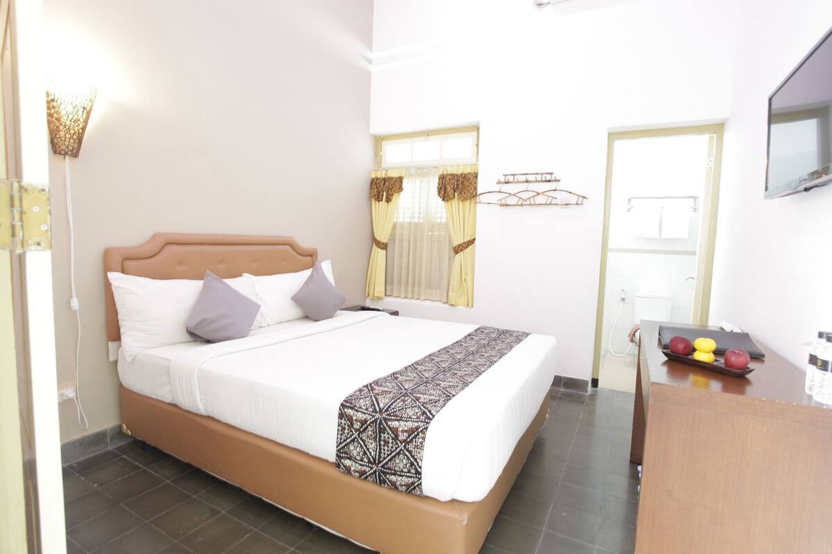 Una habitación de hotel con cama, escritorio, espejo y ventana con cortinas.